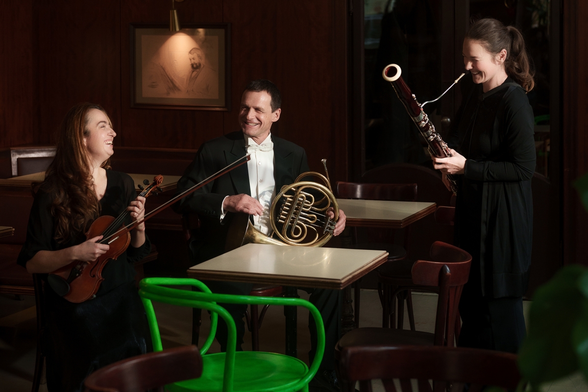 2 Frauen und 1 Mann mit Instrumenten, in der Mitte des Bildes ein grüner Stuhl