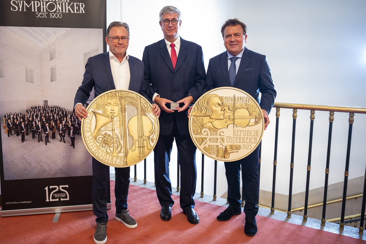 Drei Herren präsentieren eine Münze