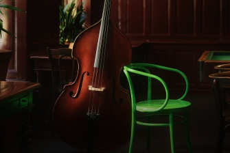foto eines großen Streichinstruments das an einem grünen Stuhl lehnt.