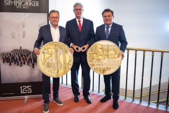 Drei Herren präsentieren eine Münze