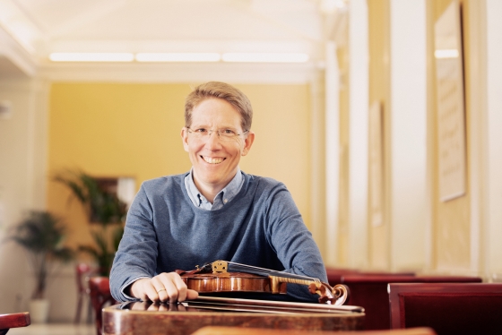 Foto von Alexander Burggasser, vor ihm liegt ein Streichinstrument auf einem Tisch